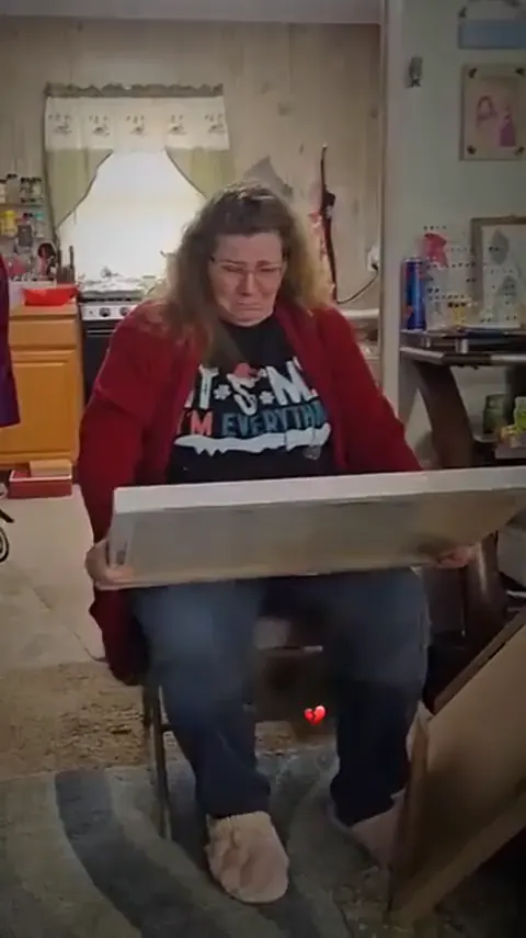 A woman in a red cardigan holding a canvas portrait, in tears.