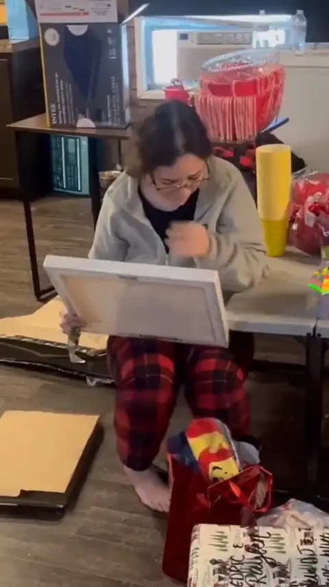 A woman in pajamas holding a canvas portrait, in tears.