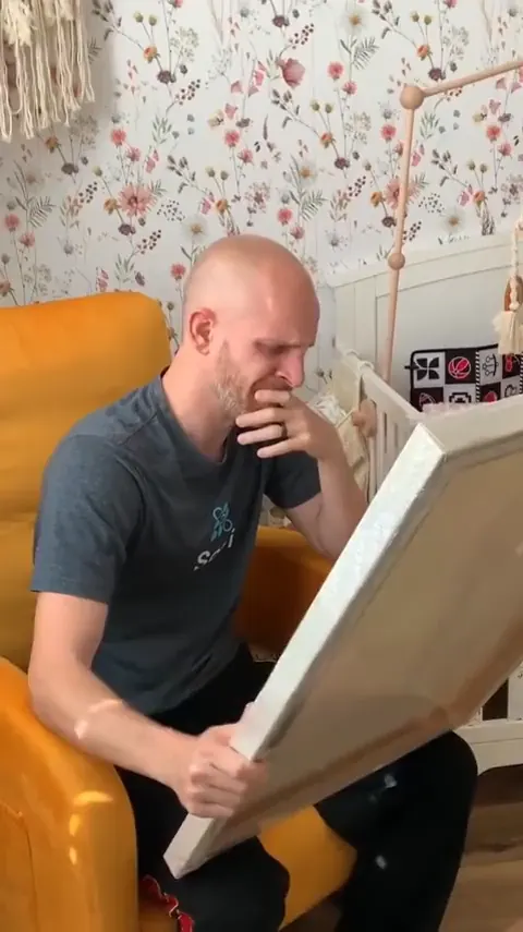 A man in a nursery holding a canvas portrait, in tears.