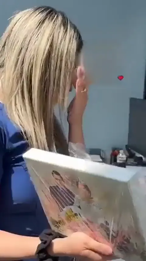 A woman in scrubs crying over a canvas portrait before a hug.
